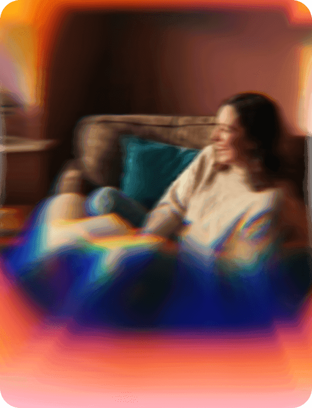 Person relaxing on couch with a book, smiling softly in warm lighting.