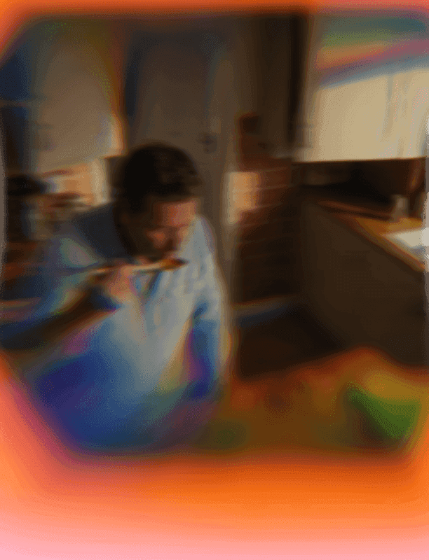 Abstract photo of a person tasting food from a spoon in a colorful, blurry kitchen.
